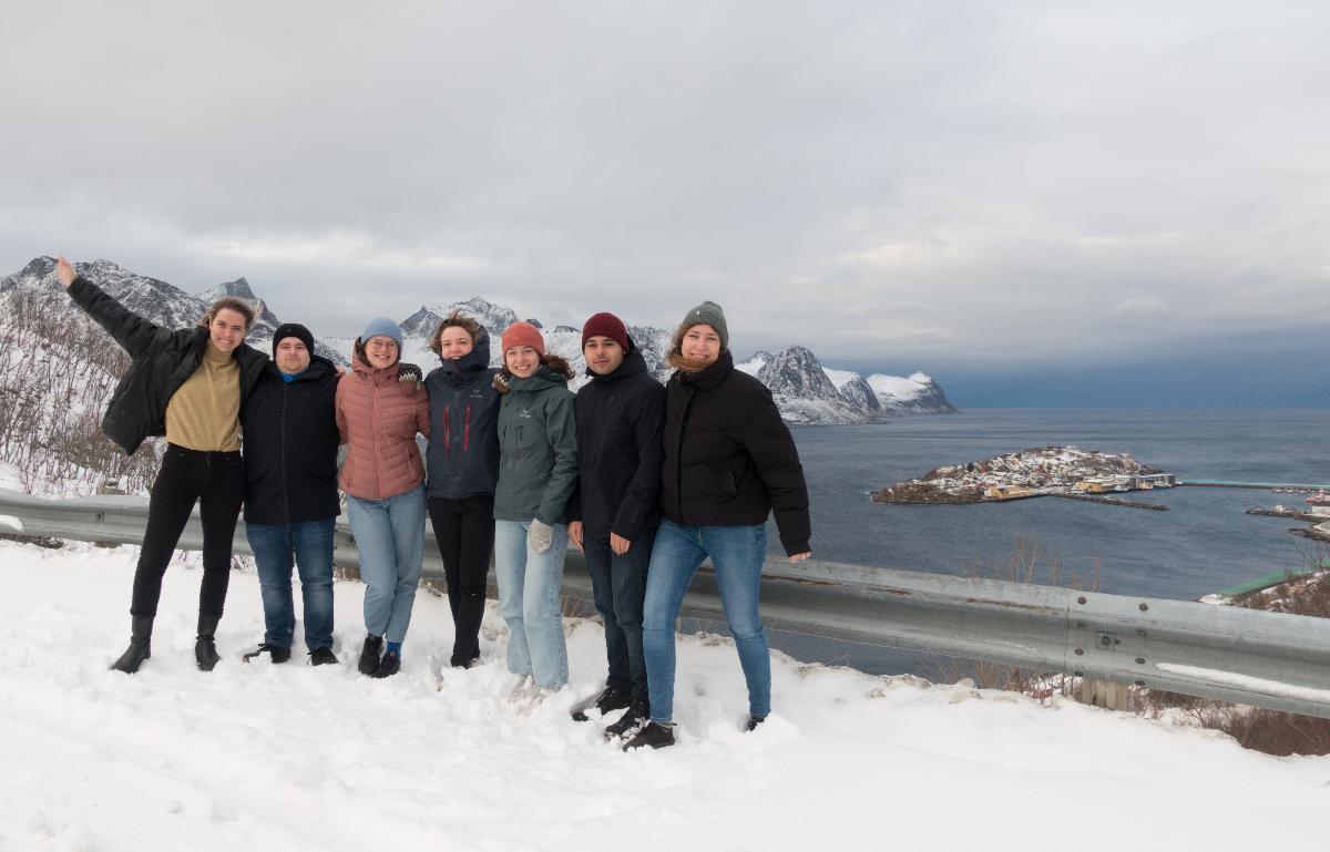 Forskere og studenter står på en vei på vinteren. I bakgrunnen, Husøy.
